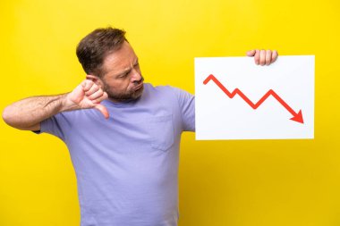 Orta yaşlı, sarı arka planda izole edilmiş beyaz bir adam elinde azalan bir istatistik ok sembolü olan ve kötü sinyal veren bir tabela tutuyor.