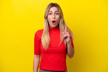 Genç Uruguaylı kadın sarı arka planda izole edilmiş bir şekilde parmağını kaldırarak çözümü anlamaya çalışıyor.