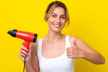 Uruguaylı genç bir kadın elinde saç kurutma makinesiyle Don sarı arka planı başparmaklarıyla izole ediyor çünkü iyi bir şey oldu.