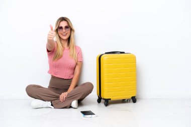 Uruguaylı gezgin kadın beyaz arka planda izole bir şekilde oturuyor. Başparmakları havada çünkü iyi bir şey oldu.