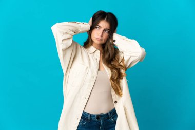 Mavi arka planda izole edilmiş genç beyaz kadın hayal kırıklığına uğramış ve kulaklarını kapatmış.