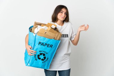 Beyaz arka planda izole edilmiş bir şekilde geri dönüşüm için elinde kağıt dolu bir geri dönüşüm çantası tutan genç bir kadın el kaldırırken şüphe duyuyor.