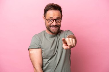 Pembe arka planda izole edilmiş yara bandı takan orta yaşlı bir adam kendine güvenen bir ifadeyle sana parmak basıyor.