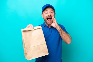 Orta yaşlı bir adam mavi arka planda izole edilmiş bir paket yiyecek alıyor ve ağzı açık bağırıyor.