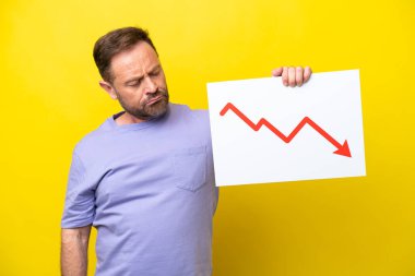 Orta yaşlı, beyaz bir adam sarı arka planda izole edilmiş. Elinde elinde, üzerinde azalan istatistik okuyla hüzünlü bir ifade olan bir işaret var.