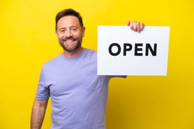 Sarı arka planda izole edilmiş orta yaşlı beyaz bir adam elinde mutlu bir ifadeyle açık bir pankart tutuyor.