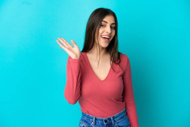 Mavi arka planda izole edilmiş beyaz bir kadın. Mutlu bir ifadeyle selamlıyor.