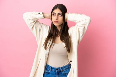 Pembe arka planda izole edilmiş genç beyaz kadın hayal kırıklığına uğramış ve kulaklarını kapatmış.