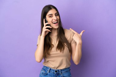 Mor arka planda izole edilmiş cep telefonu kullanan beyaz bir kadın baş parmak işareti yapıyor.