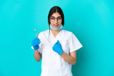 Young caucasian dentist woman holding tools isolated on blue background with surprise facial expression