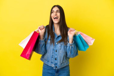 Mavi arka planda izole edilmiş genç beyaz bir kadın alışveriş torbaları tutuyor ve gülümsüyor.