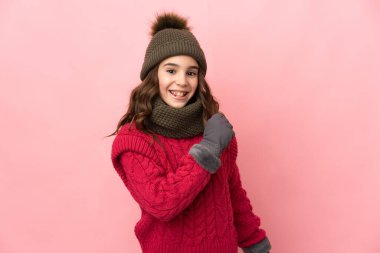 Pembe arka planda izole edilmiş, kış şapkalı küçük kız zaferi kutluyor.