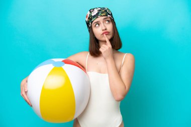 Genç Ukraynalı bir kadın elinde kumsal topu tutarken mavi arka planda izole edilmiş.
