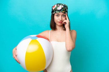 Plaj topu tutan genç Ukraynalı kadın mavi arka planda izole edilmiş bir fikir düşünüyor.