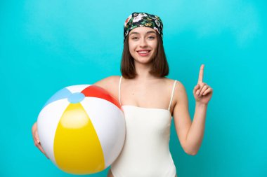 Elinde plaj topu tutan genç Ukraynalı bir kadın mavi arka planda izole edilmiş harika bir fikre işaret ediyor.