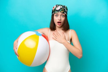 Elinde plaj topu tutan genç Ukraynalı kadın mavi arka planda izole edilmiş sağa bakarken şaşırmış ve şok olmuştu.