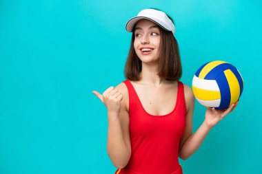 Genç Ukraynalı bir kadın, plajda voleybol oynuyor. Mavi arka planda izole edilmiş, bir ürünü sunmak için kenarı işaret ediyor.