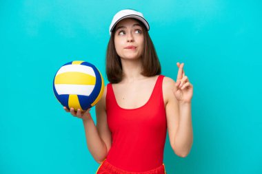 Genç Ukraynalı bir kadın, plajda voleybol oynuyor. Mavi arka planda izole edilmiş, parmaklarını çapraz yapıp en iyisini diliyor.