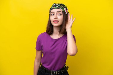 Sarı arka planda izole edilmiş genç Ukraynalı bir kadın elini kulağına koyarak bir şeyler dinliyor.