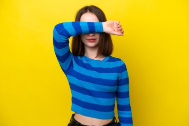 Ukraynalı genç bir kadın sarı arka planda izole edilmiş, gözleri elle kapatılmış.