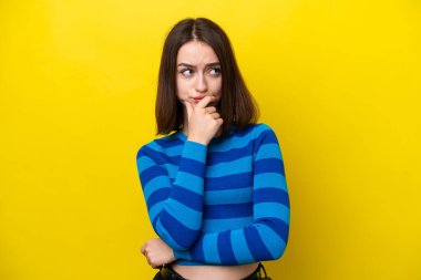 Sarı arka planda izole edilmiş genç Ukraynalı kadının şüpheleri var ve kafası karışmış bir yüz ifadesi var.