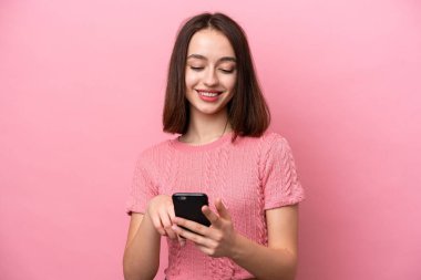 Pembe arka planda izole edilmiş genç Ukraynalı kadın cep telefonuyla mesaj ya da e-posta gönderiyor.