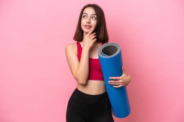 Genç sporcu Ukraynalı kadın yoga derslerine gidiyor pembe arka planda bir minder tutarken gülümserken yukarı bakıyor.