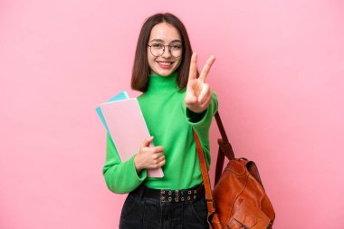 Genç öğrenci Ukraynalı kadın pembe arka planda izole edilmiş gülümsüyor ve zafer işareti gösteriyor.