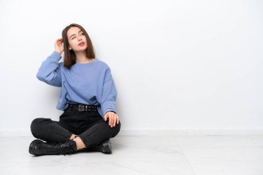 Genç Ukraynalı kadın, beyaz arka planda izole bir şekilde yerde oturuyor. Şüpheleri var ve kafası karışık.