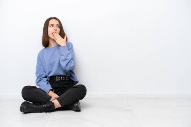 Genç Ukraynalı bir kadın beyaz arka planda izole bir şekilde yerde oturuyor esniyor ve ağzını eliyle kapatıyor.