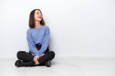 Genç Ukraynalı bir kadın beyaz arka planda izole bir şekilde yerde oturuyor ve yan yana gülüyor.