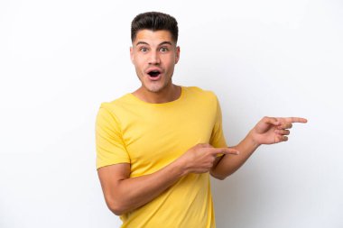 Beyaz arka planda izole edilmiş genç beyaz adam şaşırmış ve işaret ediyor.