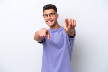 Beyaz arka planda izole edilmiş genç beyaz adam mutlu bir ifadeyle ön tarafı işaret ediyor.