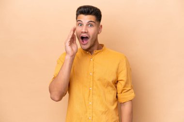 Beyazlı genç bir adam bej arka planda izole edilmiş, şaşırmış ve şok olmuş bir yüz ifadesi var.