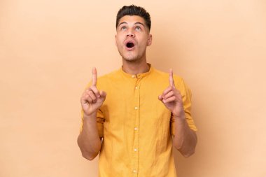 Beyazlı genç adam bej arka planda izole edilmiş şaşırmış ve yukarı bakıyor.