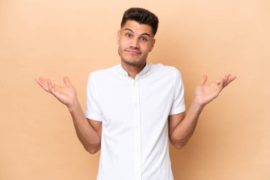 Beyazlı genç bir adam bej arka planda izole edilmiş. El kaldırırken şüphe duyuyor.