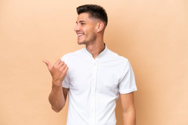Beyazların arka planında izole edilmiş genç beyaz bir adam bir ürün sunmak için kenarı işaret ediyor.