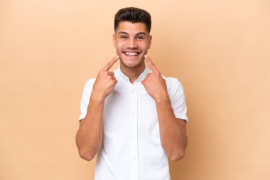 Beyaz tenli genç adam bej arka planda izole edilmiş mutlu ve hoş bir ifadeyle gülümsüyor.