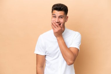Beyazlı genç bir adam bej arka planda izole edilmiş mutlu ve gülümseyen bir ağızla elini kapatıyor.