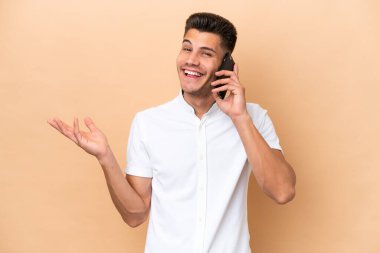 Beyazlı genç bir adam bej arka planda izole edilmiş. Cep telefonuyla sohbet ediyor.