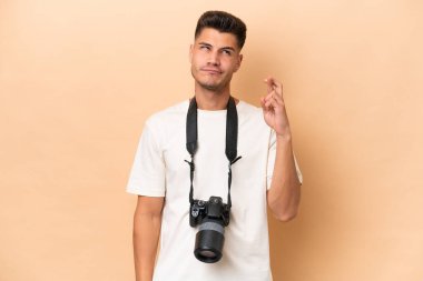 Genç fotoğrafçı beyaz adam bej arka planda izole edilmiş ve şans diliyor.