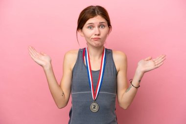 Pembe arka planda madalyaları olan genç bir İngiliz kadının ellerini kaldırırken şüpheleri var.