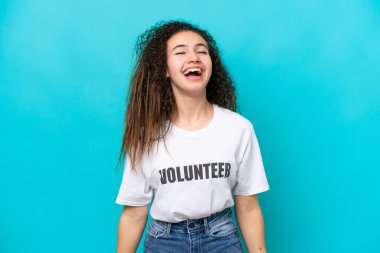 Genç Arap gönüllü kadın mavi arka planda yalnız gülüyor.