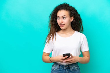 Genç bir Arap kadın mavi arka planda cep telefonu kullanarak izole edilmiş.