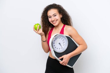 Beyaz arka planda, tartı makinesi ve elmayla izole edilmiş genç bir Arap kadın.