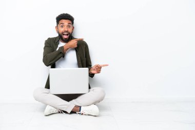 Yerde dizüstü bilgisayarı olan genç Brezilyalı bir adam izole edilmiş, beyaz şaşırmış ve işaret ediyor.