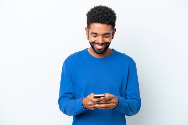 Genç Brezilyalı bir adam beyaz arka planda izole edilmiş cep telefonuyla mesaj gönderiyor.