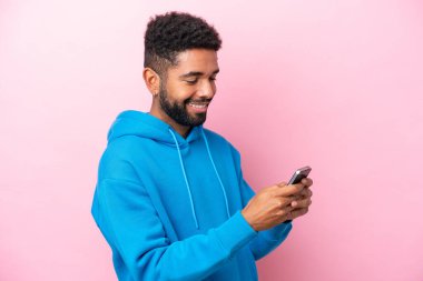 Pembe arka planda izole edilmiş genç Brezilyalı cep telefonuyla mesaj ya da e-posta gönderiyor.