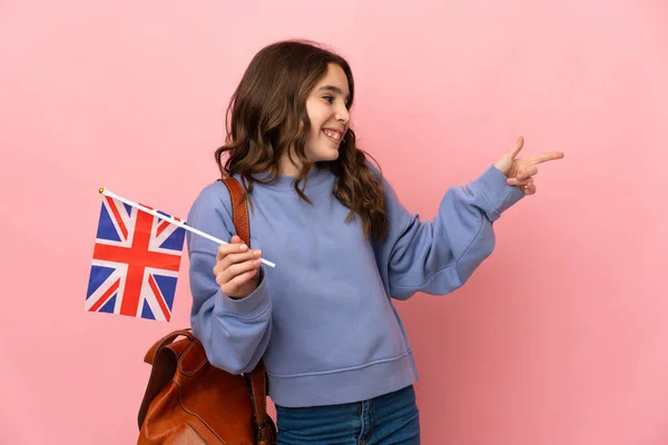 小女孩拿着一面英国国旗 用粉红的背景隔开 指指侧面 展示一种产品 — 图库照片