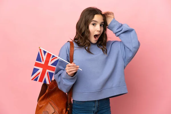 一个拿着英国国旗的小女孩 背景是粉红的 一边看着侧面 一边惊讶地做着手势 — 图库照片
